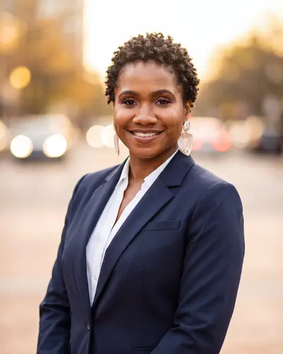 AI example made from that photo: the same woman in a navy blazer on a city street at sunset